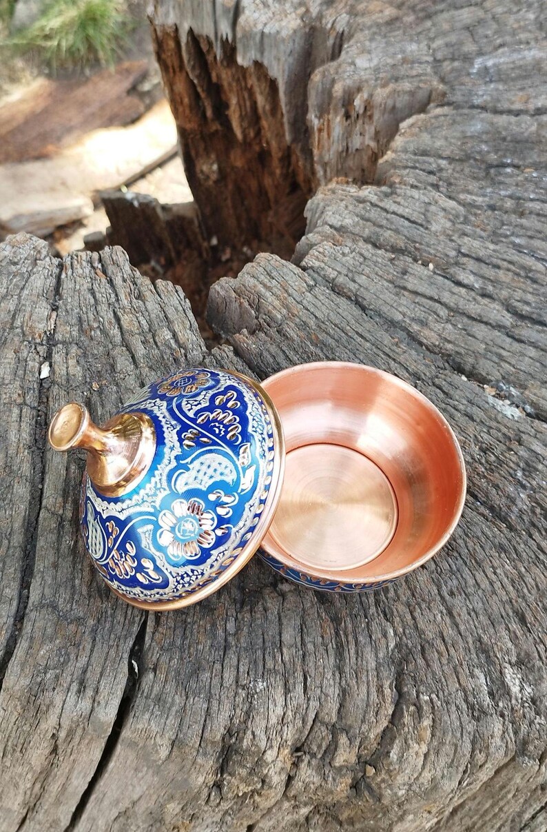 Peut inclure: Un petit bol rond en cuivre avec un couvercle assorti. L'ext&eacute;rieur du couvercle et la base du bol pr&eacute;sentent une finition en &eacute;mail bleu vif d&eacute;cor&eacute;e de motifs floraux complexes blancs et dor&eacute;s. L'int&eacute;rieur du bol est en cuivre poli.