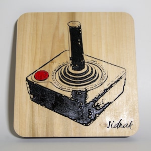 May include: A black and white illustration of a vintage joystick on a wooden surface. The joystick has a red button and the artist's signature "Sidhak" is in the bottom right corner.