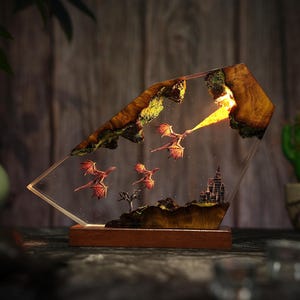 Könnte beinhalten: Fantasy-Harzlampe mit einer Drachenszene. Die Lampe hat einen Holzsockel und eine klare, abgewinkelte Harzplatte. Drei rote Drachen fliegen, einer speit Feuer. Ein Schloss und ein Baum sind ebenfalls zu sehen.