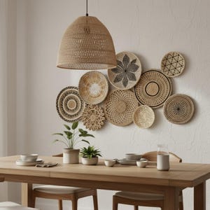 Op de afbeelding: Een eethoek met een houten tafel, gedekt met servies en planten. Boven de tafel hangt een geweven hanglamp. De muur is versierd met een verzameling geweven decoratieve borden in verschillende maten en patronen, wat een natuurlijke, bohemien sfeer creëert.