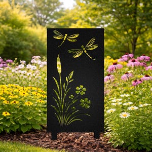 Puede incluir: Una estaca de jardín de metal negro con diseños recortados de libélulas, juncos y flores. El panel decorativo se apoya en dos patas pequeñas y está situado en un jardín con flores y vegetación coloridas.