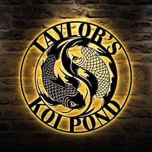 May include: A black metal sign with a circular design featuring two koi fish in a yin yang style. The text "Taylor's Koi Pond" is written around the edge of the circle.