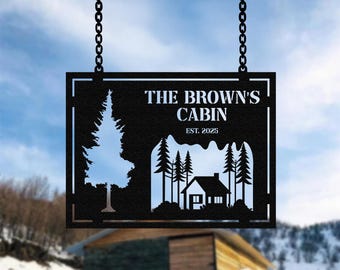 May include: Black metal cabin sign with the text "THE BROWN'S CABIN EST. 2025". The sign features a cut-out design of a tree and a cabin with trees. The sign is hanging from a wooden beam with chains.