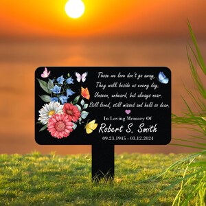 May include: A black memorial garden stake with a rectangular sign featuring a floral design and butterflies. The sign includes the text "Those we love don't go away... In Loving Memory Of Robert S. Smith 09.23.1945 - 03.12.2024."