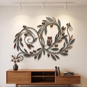 Könnte beinhalten: Eine große Wandskulptur aus Metall mit einem komplexen Design aus Olivenzweigen mit dunkelgrünen Blättern und bronzefarbenen Oliven. Eine kleine, detaillierte Eulenfigur sitzt auf einem der Zweige, integriert in die Mitte des geschwungenen Blattwerks.
