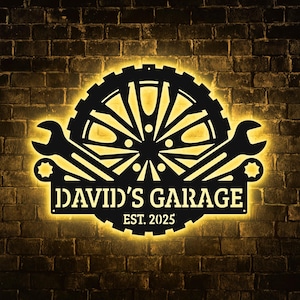 May include: Black metal garage sign with a gear and wrench design, illuminated with a warm yellow glow. The sign reads "DAVID'S GARAGE EST. 2025" against a brick wall background.