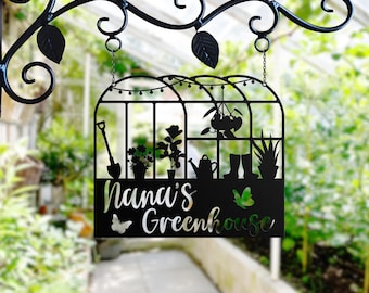 May include: Black metal sign featuring a silhouette of a greenhouse with plants, a watering can, boots, and a shovel. The sign reads "Nana's Greenhouse" with a butterfly on each side.