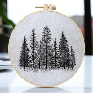 May include: A hand-stitched embroidery hoop featuring a black and white forest scene. The design showcases a collection of detailed evergreen trees against a light-colored fabric background, held within a wooden hoop.