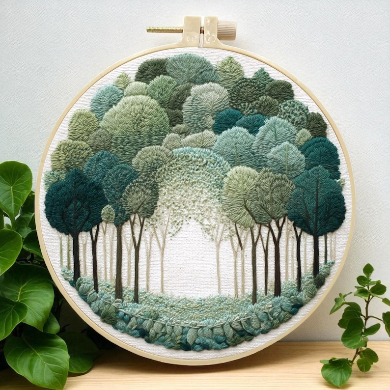 May include: A hand-stitched embroidery hoop art piece featuring a forest scene. The artwork showcases a variety of green hues, depicting trees and foliage. The embroidery is set in a round wooden hoop, creating a textured, three-dimensional effect.