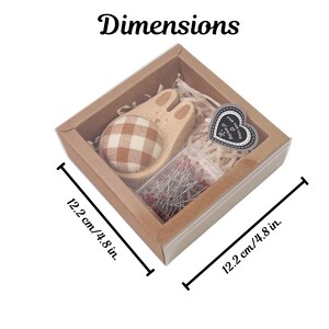 May include: A sewing kit presented in a square cardboard box, measuring 12.2 cm on each side. The kit contains a wooden bunny-shaped pin cushion with a plaid fabric ball, a small container of pins, and a heart-shaped tag that reads "For the love of sewing."
