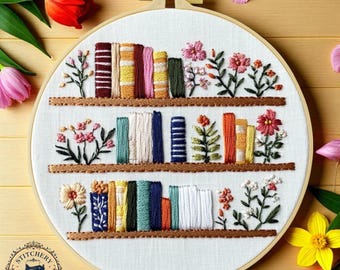 Pode incluir: Arte bordada em bastidor com um design de estante com livros coloridos e detalhes florais. A obra apresenta três prateleiras com lombadas de livros em vermelho, amarelo, verde e azul, rodeadas por flores bordadas.
