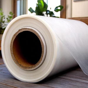 May include: A roll of clear cling film is rolled up on a cardboard core. The cling film is translucent and has a slight sheen.