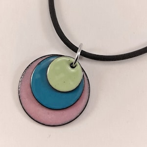 May include: A necklace with a pendant made of three overlapping circles. The circles are painted in shades of pink, teal, and light green.