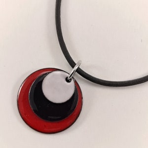 May include: A necklace with a pendant made of three overlapping circles. The circles are red, black, and white.