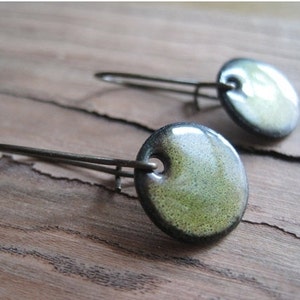 May include: A pair of green and black ceramic earrings with silver hooks. The earrings are round and have a speckled texture.