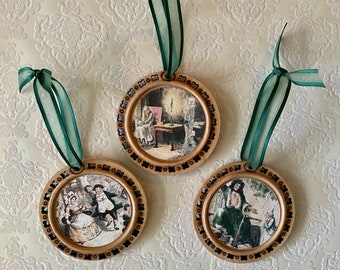 May include: Three round wooden ornaments with green ribbon hangers. Each ornament features a different vintage illustration printed on the front. The illustrations depict a man sitting at a table, a couple dancing, and a man with a staff.