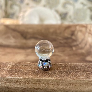 May include: A clear glass ball with a silver base decorated with iridescent rhinestones. The ball is sitting on a wooden surface.