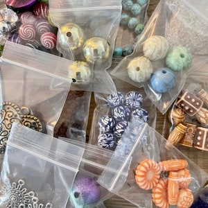 May include: Assortment of colorful beads in various shapes and sizes, packaged in clear plastic bags. The beads include turquoise, gold, silver, purple, orange, and blue.