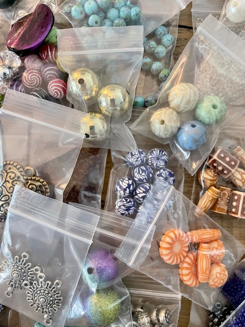 May include: Assortment of colorful beads in various shapes and sizes, packaged in clear plastic bags. The beads include turquoise, gold, silver, purple, orange, and blue.