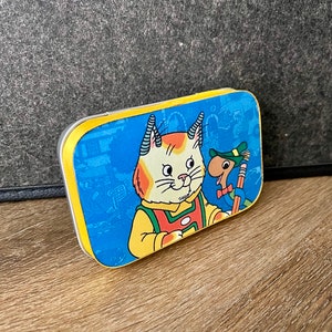 May include: A blue and yellow metal tin with a cartoon cat and a mouse on it. The cat is wearing a red and white shirt and the mouse is wearing a green hat. The tin has a yellow border.