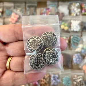 May include: Four silver-toned metal buttons with a mandala-like design. The buttons are in a clear plastic bag.