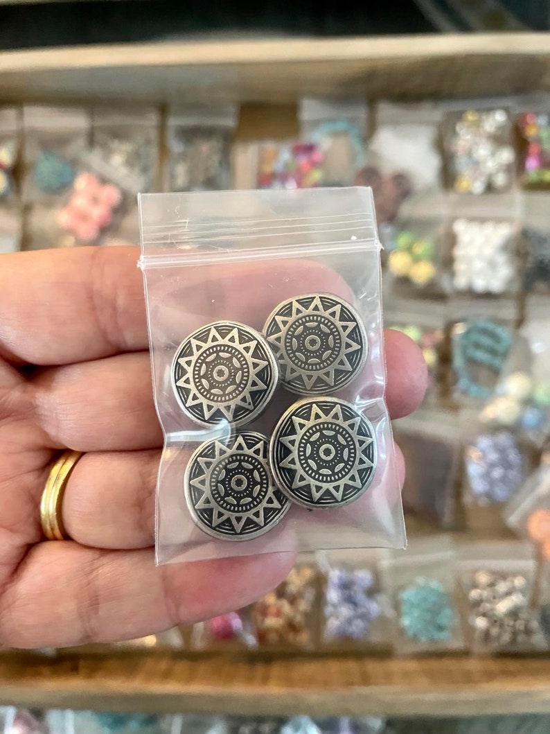May include: Four silver-toned metal buttons with a mandala-like design. The buttons are in a clear plastic bag.