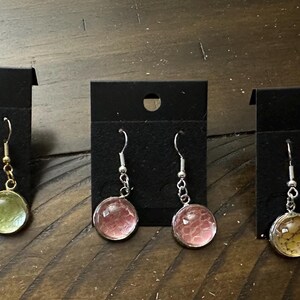 Op de afbeelding: Drie paar oorhangers met verschillende gekleurde hars cabochons. De oorhangers links hebben een lichtgroene cabochon, de oorhangers in het midden hebben een roze cabochon en de oorhangers rechts hebben een lichtbruine cabochon.