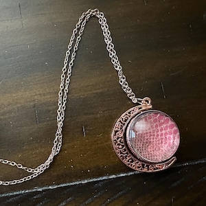 Może przedstawiać: Srebrny łańcuszek z naszyjnikiem w kształcie półksiężyca w kolorze różowego złota z ozdobną szklaną kulą w kolorze różowym i białym.