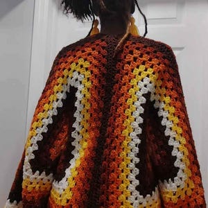 May include: A brown, orange, white, and yellow crochet cardigan with a granny square pattern.