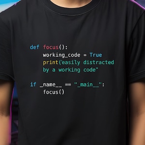 Può includere: T-shirt nero con codice di programmazione in bianco, turchese e giallo. Il codice include il testo "easily distracted by a working code". La maglietta è a girocollo e maniche corte.