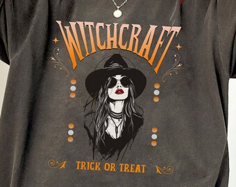 May include: A dark gray oversized t-shirt with a vintage-style graphic of a woman in a witch hat and the text "Witchcraft" and "A Trick or Treat".