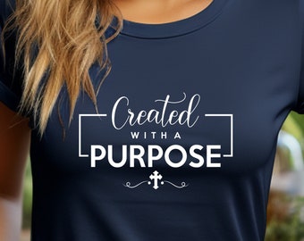 Puede incluir: Una camiseta azul marino con un gráfico blanco que dice "Creado con un propósito" y un pequeño símbolo de cruz.