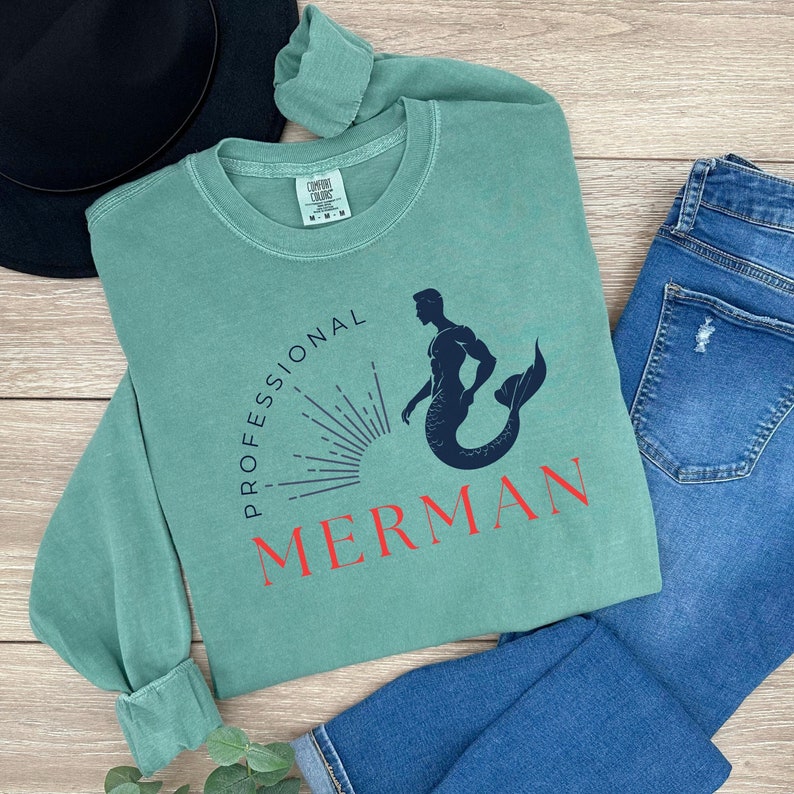 May include: A green long-sleeved shirt with a graphic of a merman with the text "Professional Merman" in red.