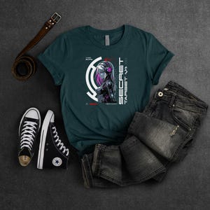 May include: A teal blue t-shirt with a graphic of a woman with pink hair and a futuristic design. The text "SECRET TARGET" is on the shirt.