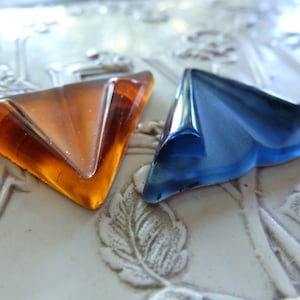 May include: Two glass triangles, one amber and one blue, on a white surface with a floral design.
