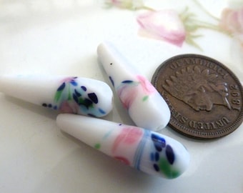 May include: Three white glass beads with a floral design in shades of pink, blue, and green.