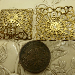 May include: Two gold-colored metal filigree squares with a decorative design. The squares are about 2 inches in size.