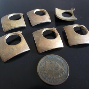 May include: Seven brass metal pieces with a square shape and a circular cutout in the center. The pieces are arranged in a random pattern on a black surface.