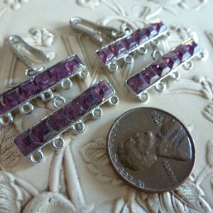 May include: Two silver-toned jewelry connectors with a row of five purple rhinestones on each side. The connectors have three loops on each side for attaching to jewelry.