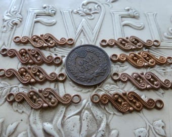 May include: Eight copper-toned metal connectors with an S-shaped scrollwork design and small circular loops at each end, arranged around a central United States one-cent coin for scale, featuring intricate embossed patterns and raised dots.
