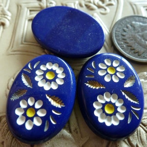 May include: Three oval-shaped glass buttons with a dark blue background and white floral designs. The flowers have yellow centers.
