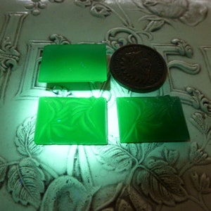 May include: Four green glass tiles, two with a floral design and two plain. The tiles are on a white surface with a floral design.