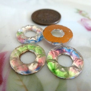 May include: Four iridescent glass rings with a variety of colors, including pink, blue, green, and orange. The rings are all the same size and shape, and they are arranged in a circle.
