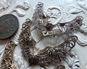 May include: Three antique metal filigree pieces in a crescent shape. The pieces are made of a light gold metal and have intricate designs.