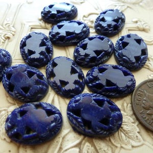 May include: A collection of twelve oval-shaped, deep blue lapis lazuli cabochons featuring intricate carved floral and leaf motifs, displayed alongside a copper-colored 1895 United States Indian Head cent coin for scale.
