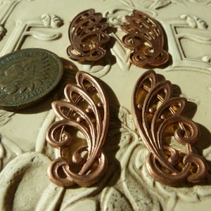 May include: Four copper-colored metal filigree embellishments with intricate floral designs. The embellishments are on a white surface.