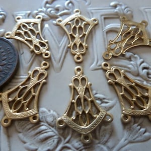 May include: Six gold-tone metal decorative embellishments with intricate designs. Each embellishment has three holes for attaching to a project.