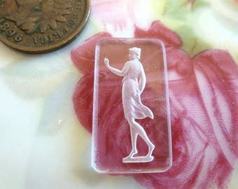 May include: A clear glass cameo with a white raised image of a woman in a flowing dress. The cameo is rectangular and has a slightly frosted appearance.