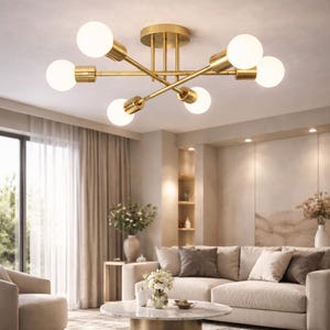 Op de afbeelding: Een moderne goudkleurige plafondlamp met zes bolvormige lampen. De lamp heeft een Sputnik-ontwerp met armen die zich uitstrekken vanuit een centrale basis. De lampen zijn wit en de armatuur is geïnstalleerd in een woonkamer.