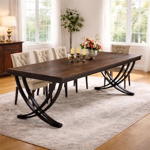 Peut inclure: Une table de salle à manger rectangulaire marron foncé avec des pieds croisés en métal noir. Des chaises beige rembourrées entourent la table. Un vase de fleurs et des bougies ornent la table, dans une pièce lumineuse avec de grandes fenêtres.